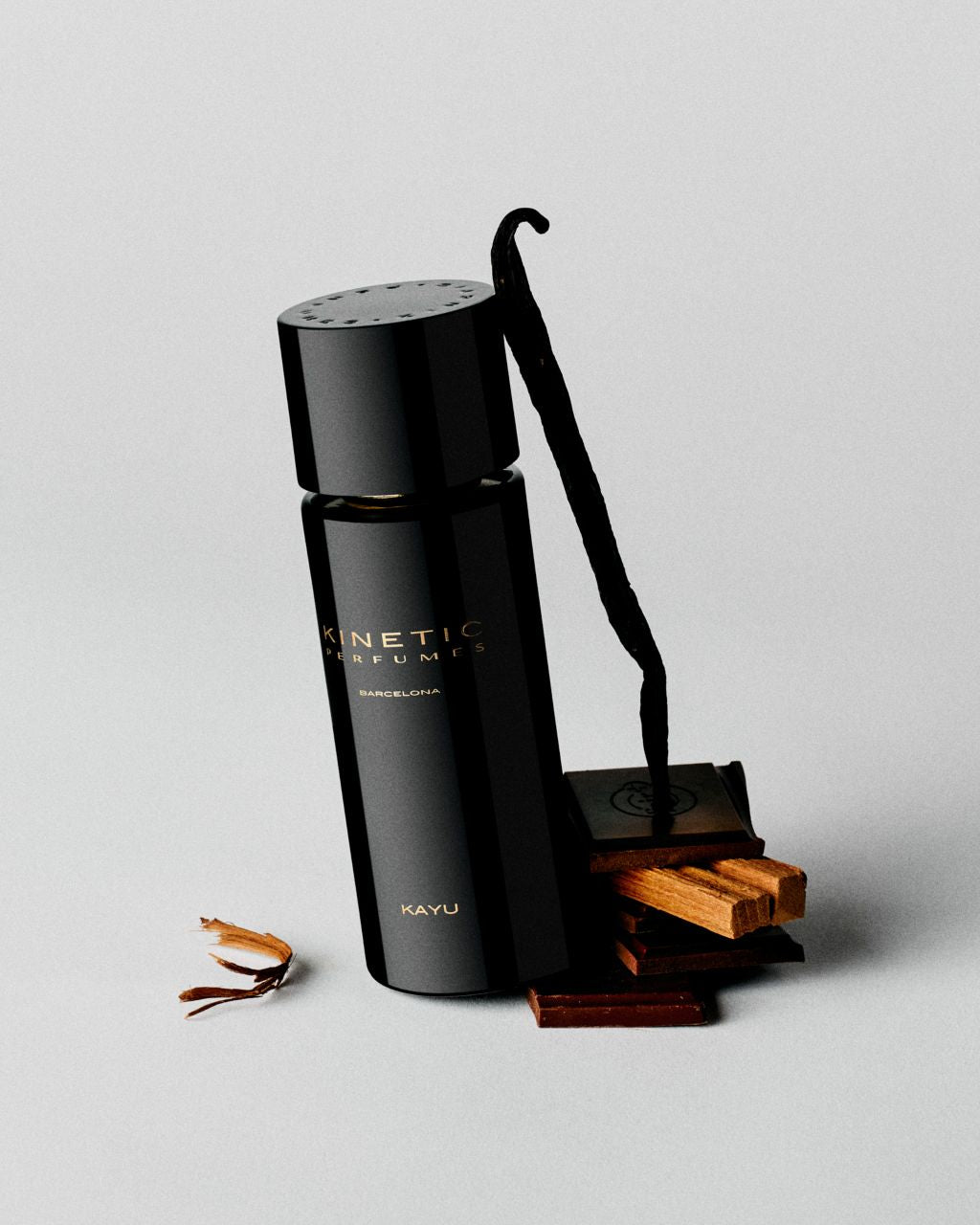Kinetic Perfumes Kayu Extrait de Parfum 100 ml – schwarzer Flakon mit Vanilleschote, Schokolade und Holzstücken auf Hellgrau
