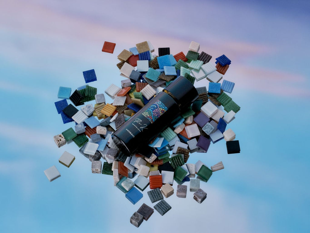 Kinetic Perfumes Mosaic Extrait de Parfum 100 ml – liegender Flakon auf Haufen bunter Mosaiksteine vor Himmel