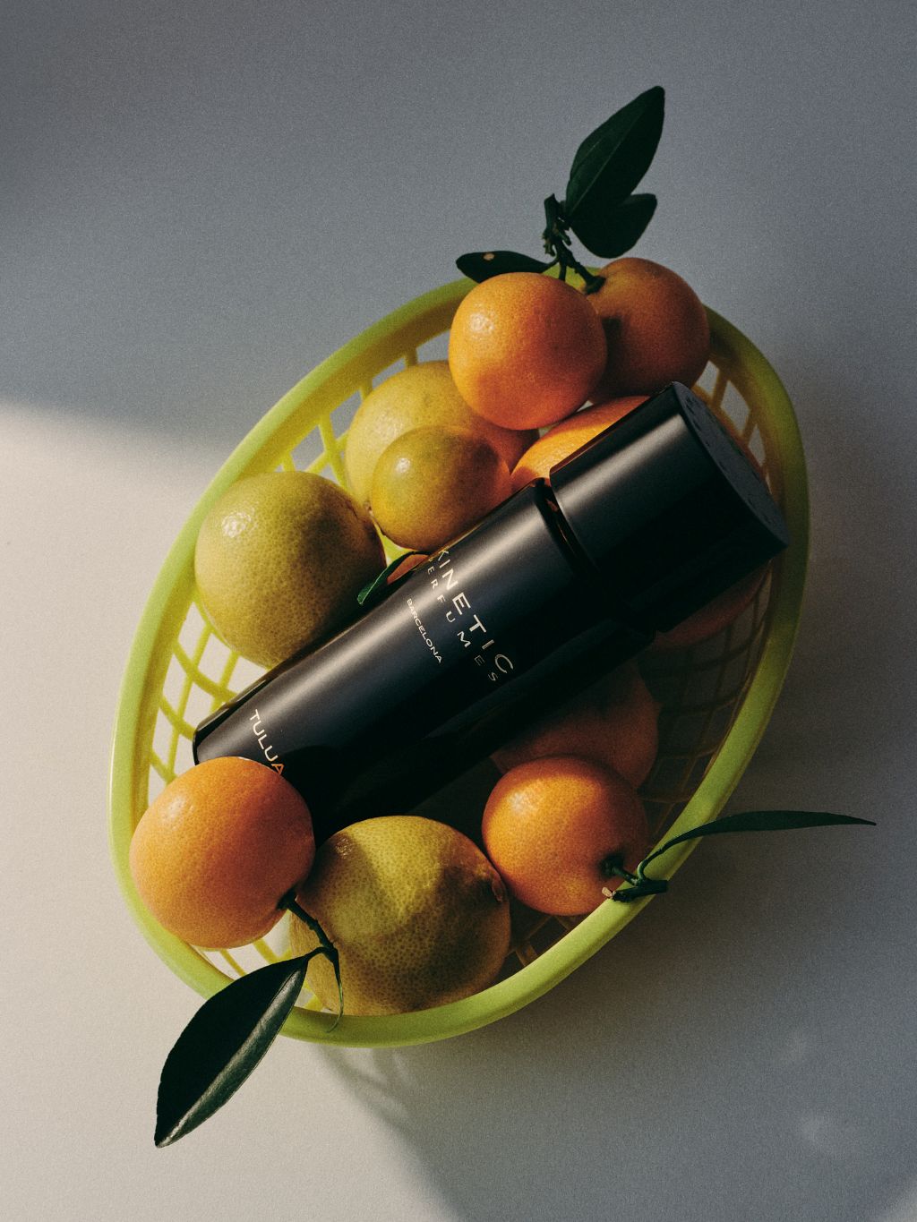 Kinetic Perfumes Tulua Extrait de Parfum 100 ml – liegender schwarzer Flakon in gelbgrünem Korb mit Mandarinen und Limetten