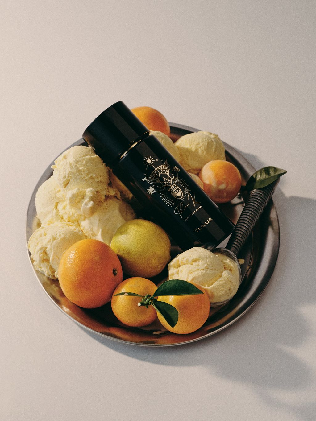 Kinetic Perfumes Tulua Extrait de Parfum 100 ml – liegender Flakon auf Silberteller mit Vanilleeis und Zitrusfrüchten