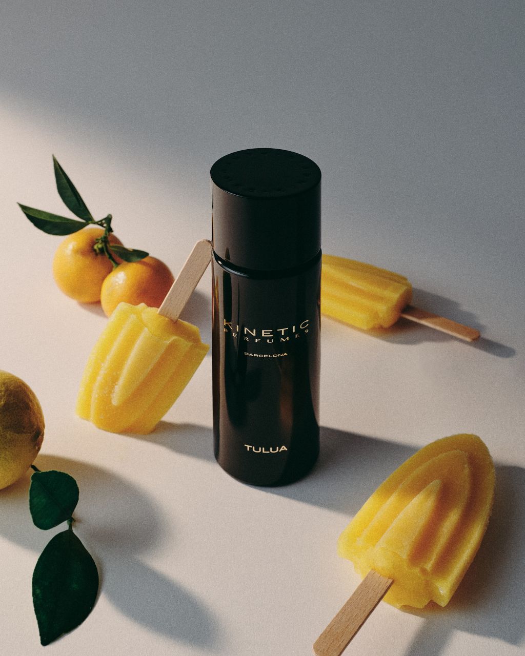 Kinetic Perfumes Tulua Extrait de Parfum 100 ml – schwarzer Flakon zwischen gelbem Wassereis und Mandarinen auf hellem Grund