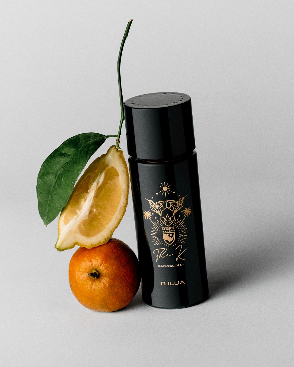Kinetic Perfumes Tulua Extrait de Parfum 100 ml – Flakon mit goldenem Emblem neben Zitronenschnitz und Mandarine auf Hellgrau