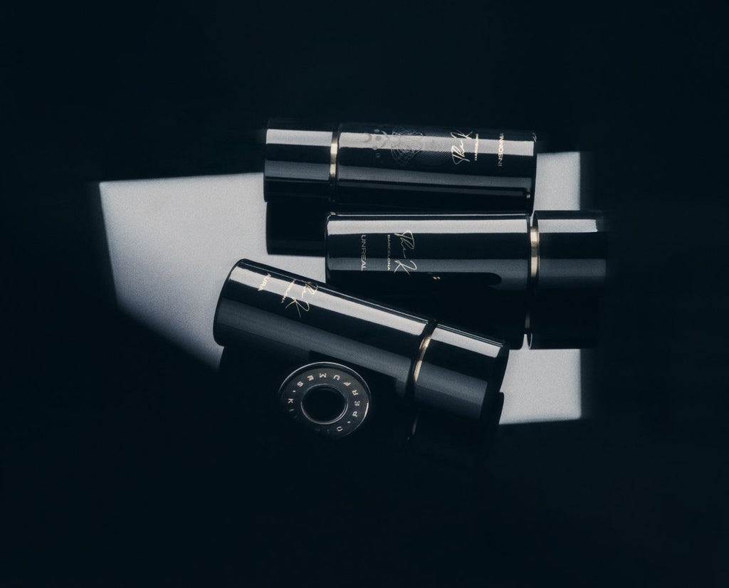Kinetic Perfumes Unreal Extrait de Parfum 100 ml – drei liegende schwarze Flakons mit Kappe auf weissem Lichtfeld vor Schwarz