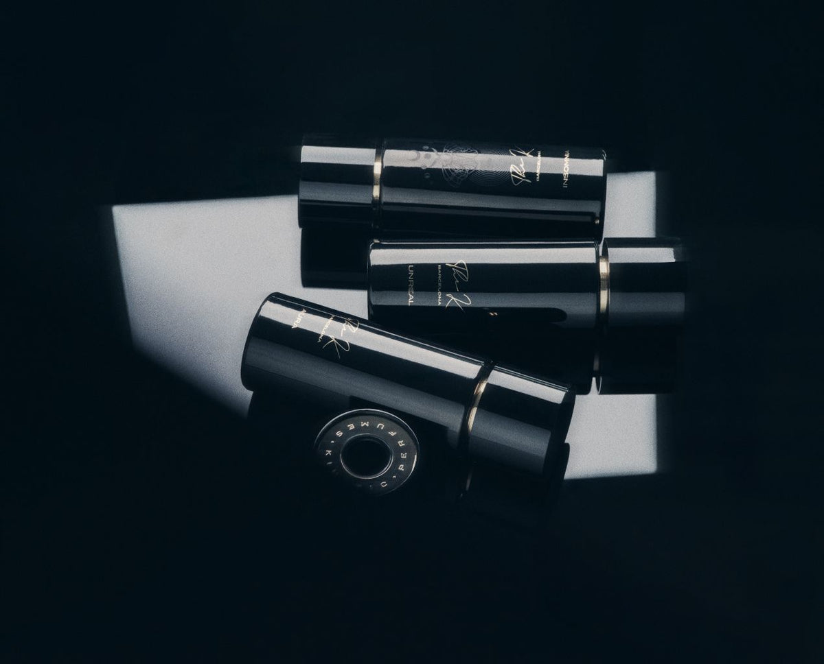 Kinetic Perfumes Unreal Extrait de Parfum 100 ml – drei liegende schwarze Flakons mit Kappe auf weissem Lichtfeld vor Schwarz