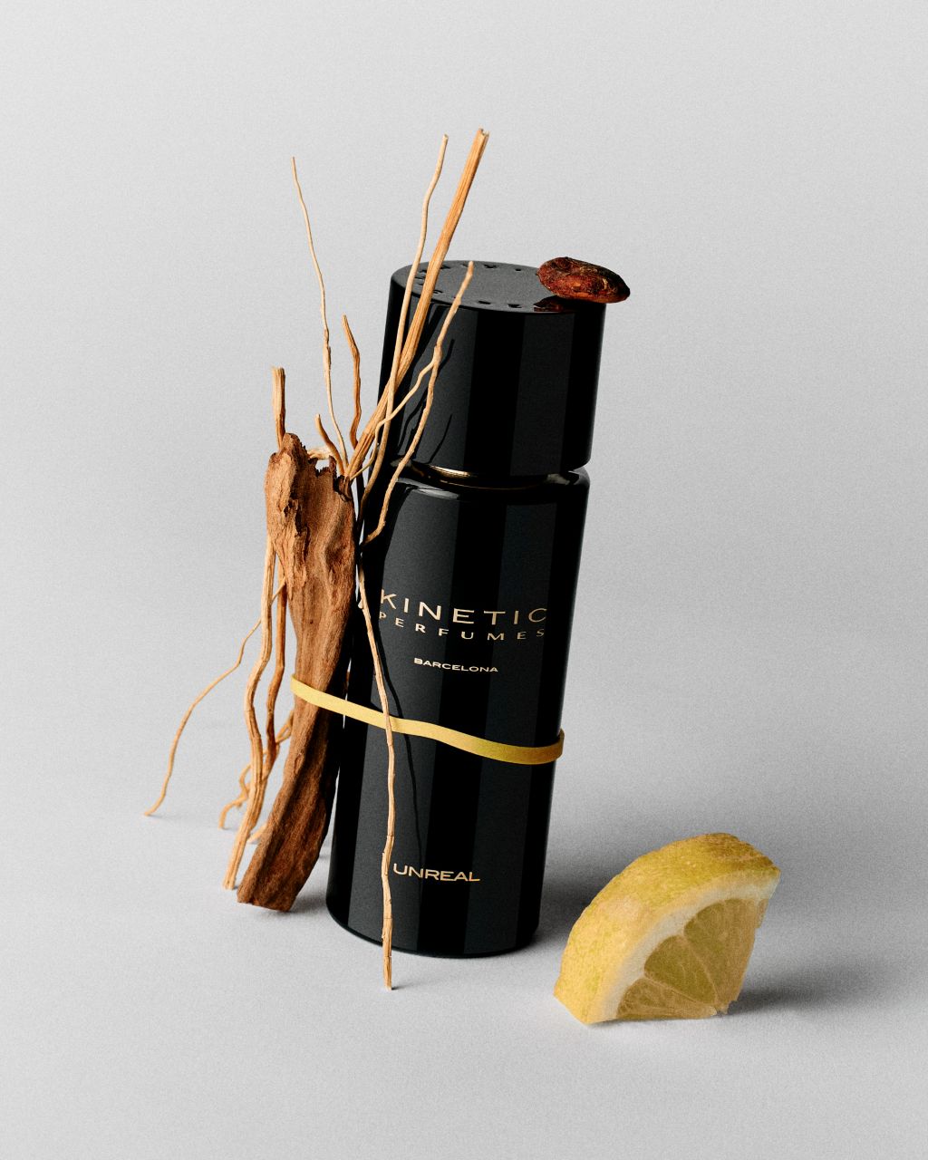 Kinetic Perfumes Unreal Extrait de Parfum 100 ml – schwarzer Flakon mit Holzspänen, gelbem Band und Zitronenschnitz auf Hellgrau