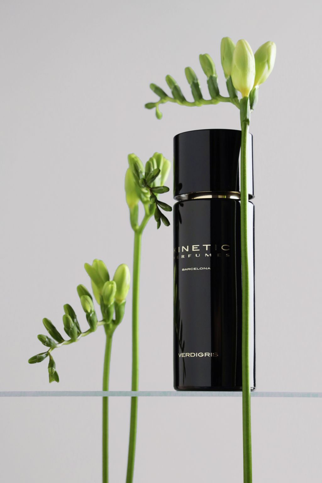 Kinetic Perfumes Verdigris Extrait de Parfum 100 ml – schwarzer Flakon mit grünen Freesienknospen auf Glasplatte vor Hellgrau