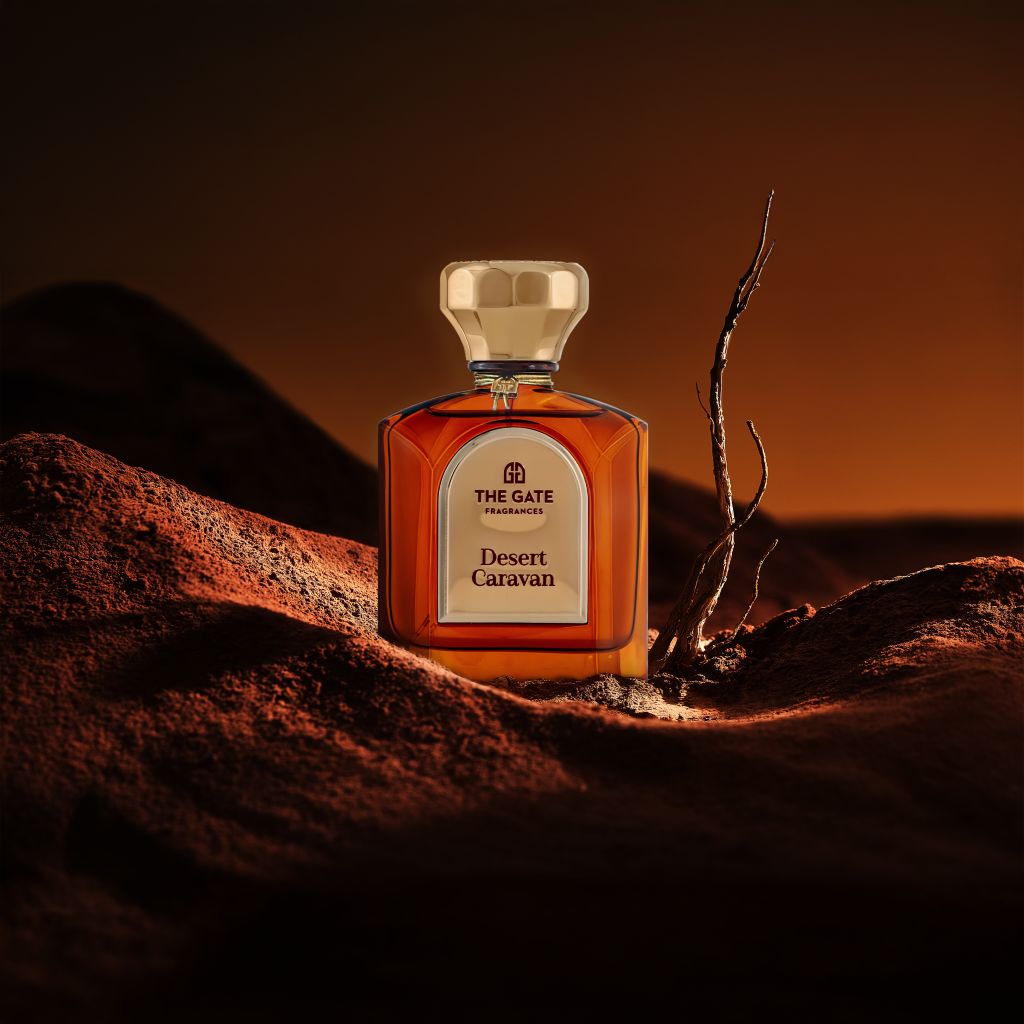 The Gate Desert Caravan Extrait de Parfum 100 ml – bernsteinfarbener Flakon auf rotbraunen Dünen mit kahlem Ast in der Dämmerung