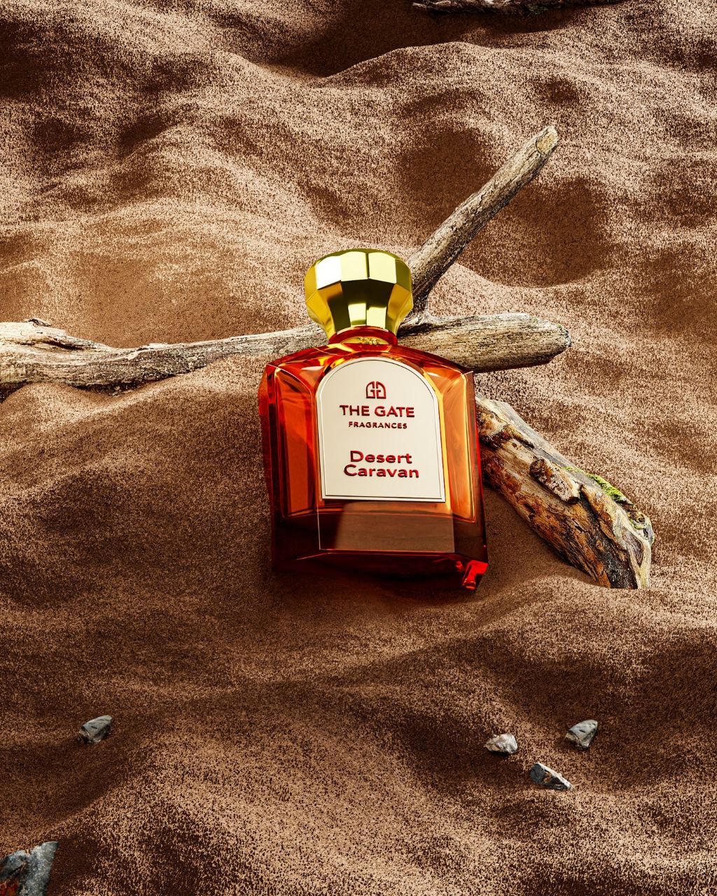 The Gate Desert Caravan Extrait de Parfum 100 ml – orangeroter Flakon mit roter Etikettschrift liegend im Sand mit Treibholz