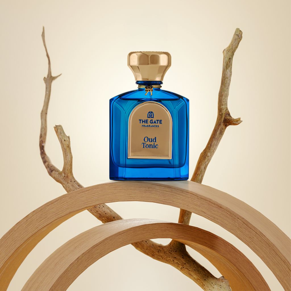 The Gate Oud Tonic Extrait de Parfum 100 ml – blauer Flakon auf Holzbögen mit Treibholzast vor beigem Hintergrund