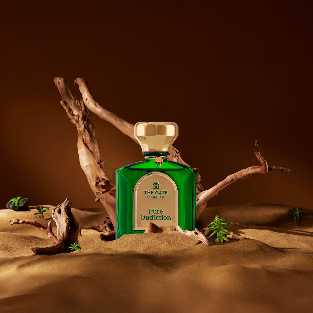 The Gate Pure Oudiction Extrait de Parfum 100 ml – grüner Flakon im Sand mit Treibholz vor braunem Hintergrund