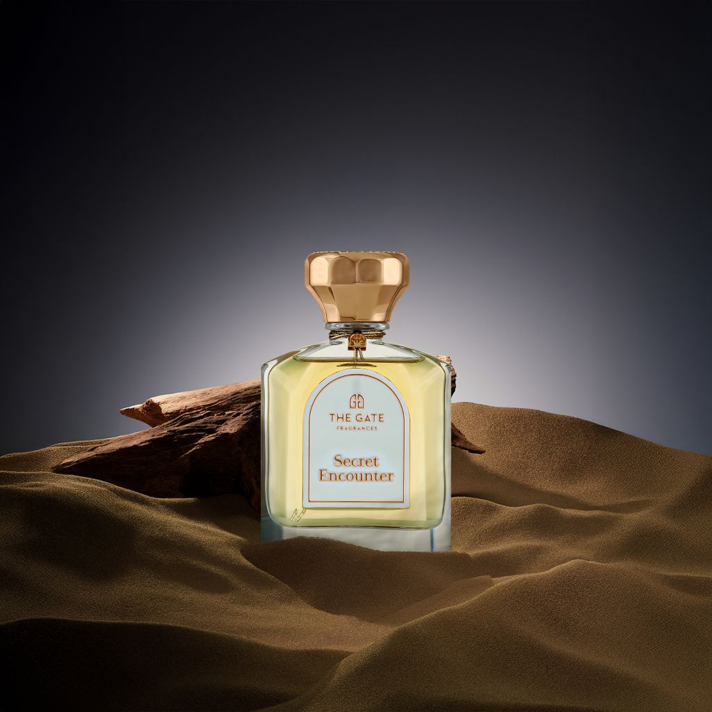The Gate Secret Encounter Extrait de Parfum 100 ml – hellgoldener Flakon in braunen Sanddünen mit Treibholz vor dunklem Hintergrund