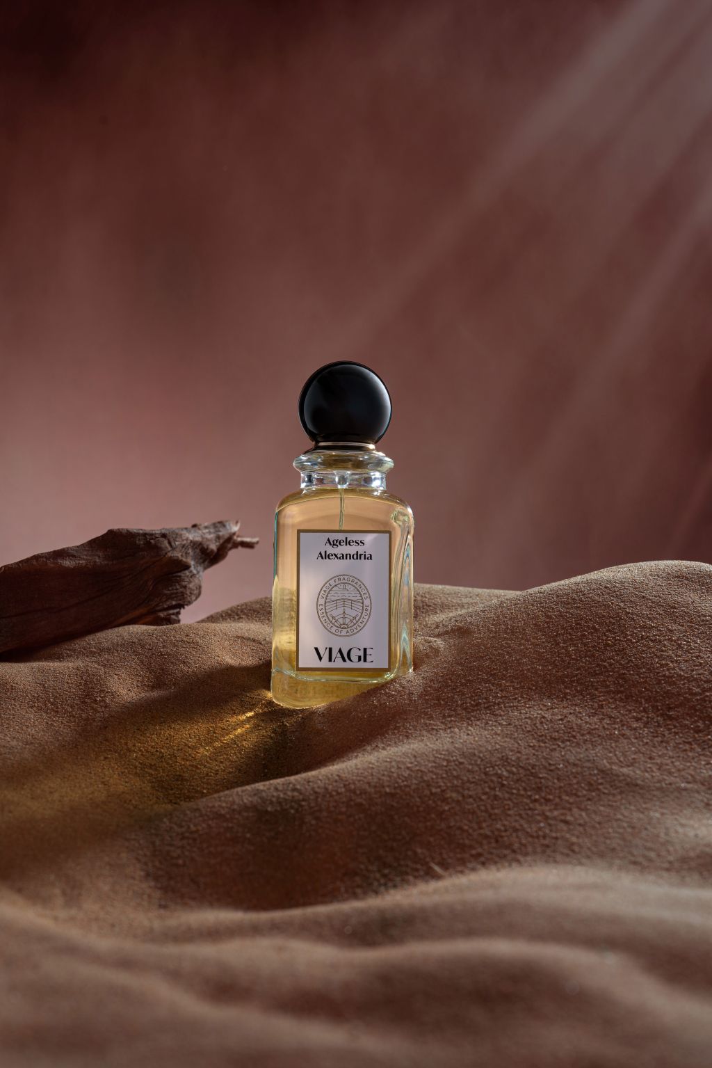 Viage Ageless Alexandria Extrait de Parfum 100 ml – Flakon auf sandfarbenem Wildleder mit Treibholz vor rotbraunem Hintergrund
