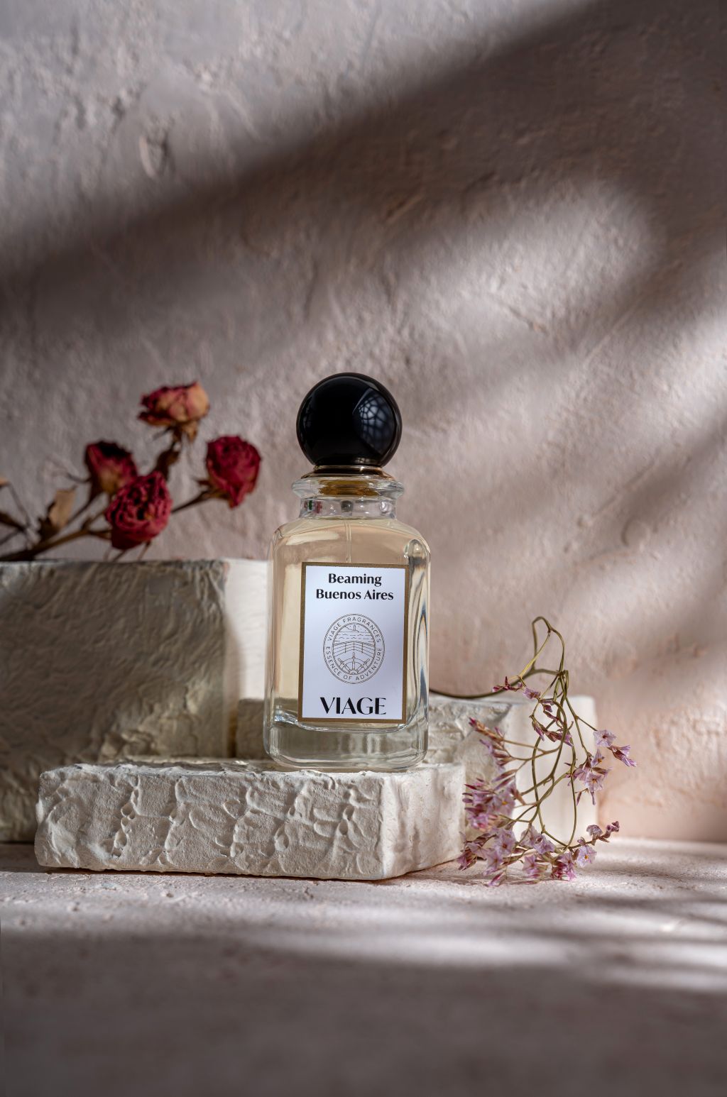 Viage Beaming Buenos Aires Extrait de Parfum 100 ml – Flakon auf weissem Steinblock mit Trockenrosen und Strandflieder vor heller Wand