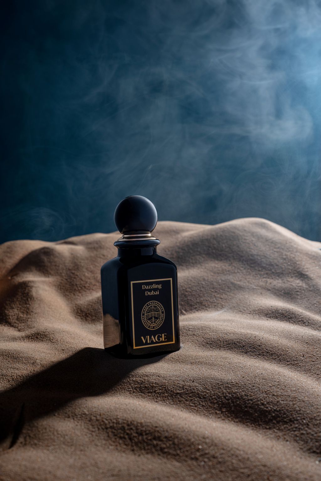 Viage Dazzling Dubai Extrait de Parfum 100 ml – Schwarzer Flakon in Sanddüne vor dunkelblauem Hintergrund mit Rauch
