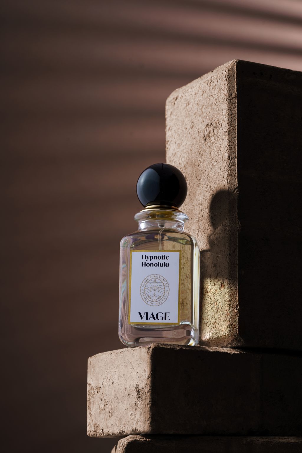 Viage Hypnotic Honolulu Extrait de Parfum 100 ml – Flakon auf Sandsteinblöcken mit Streifenschatten vor brauner Wand