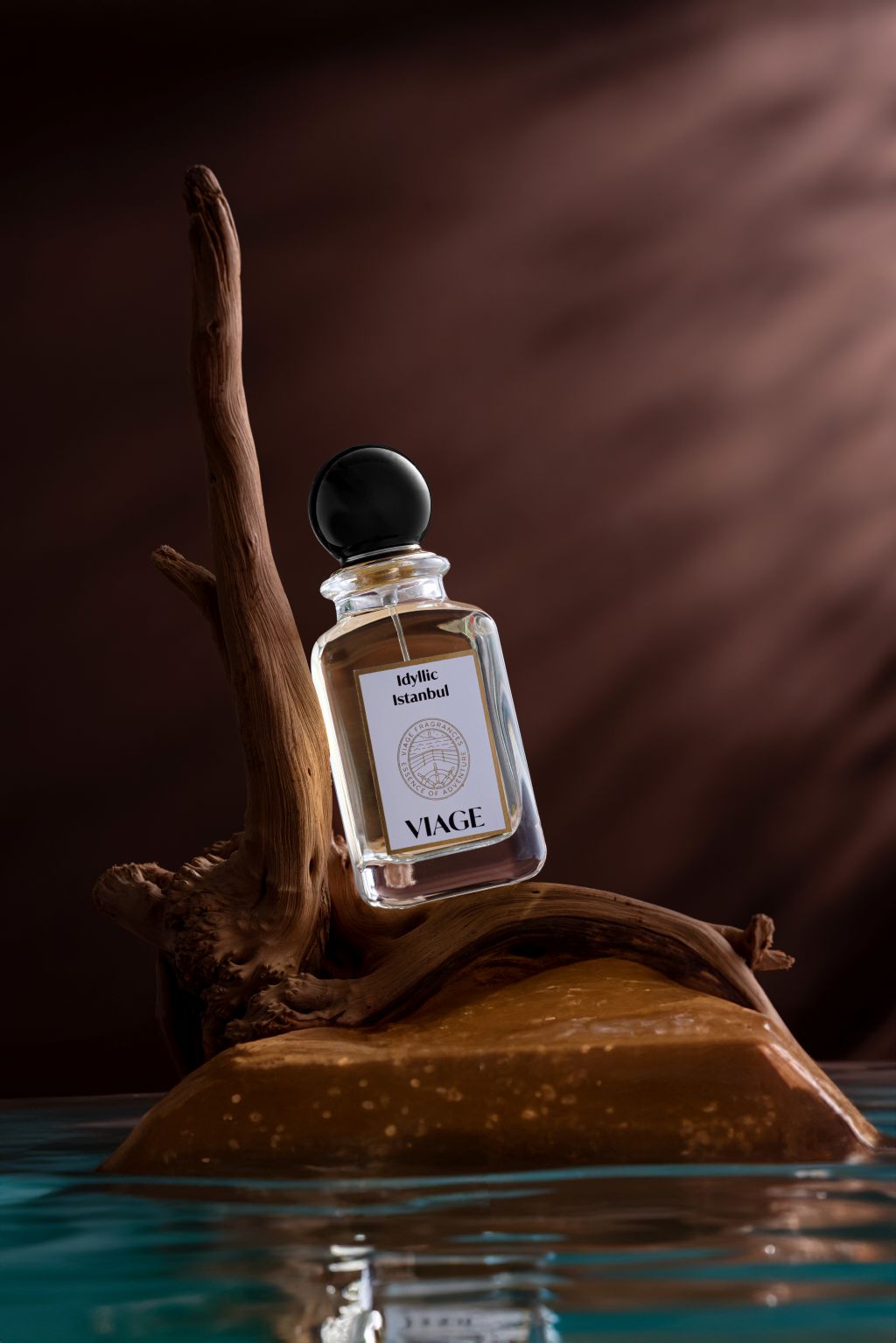 Viage Idyllic Istanbul Extrait de Parfum 100 ml – Flakon schräg auf Treibholz über Wasser vor dunkelbraunem Hintergrund