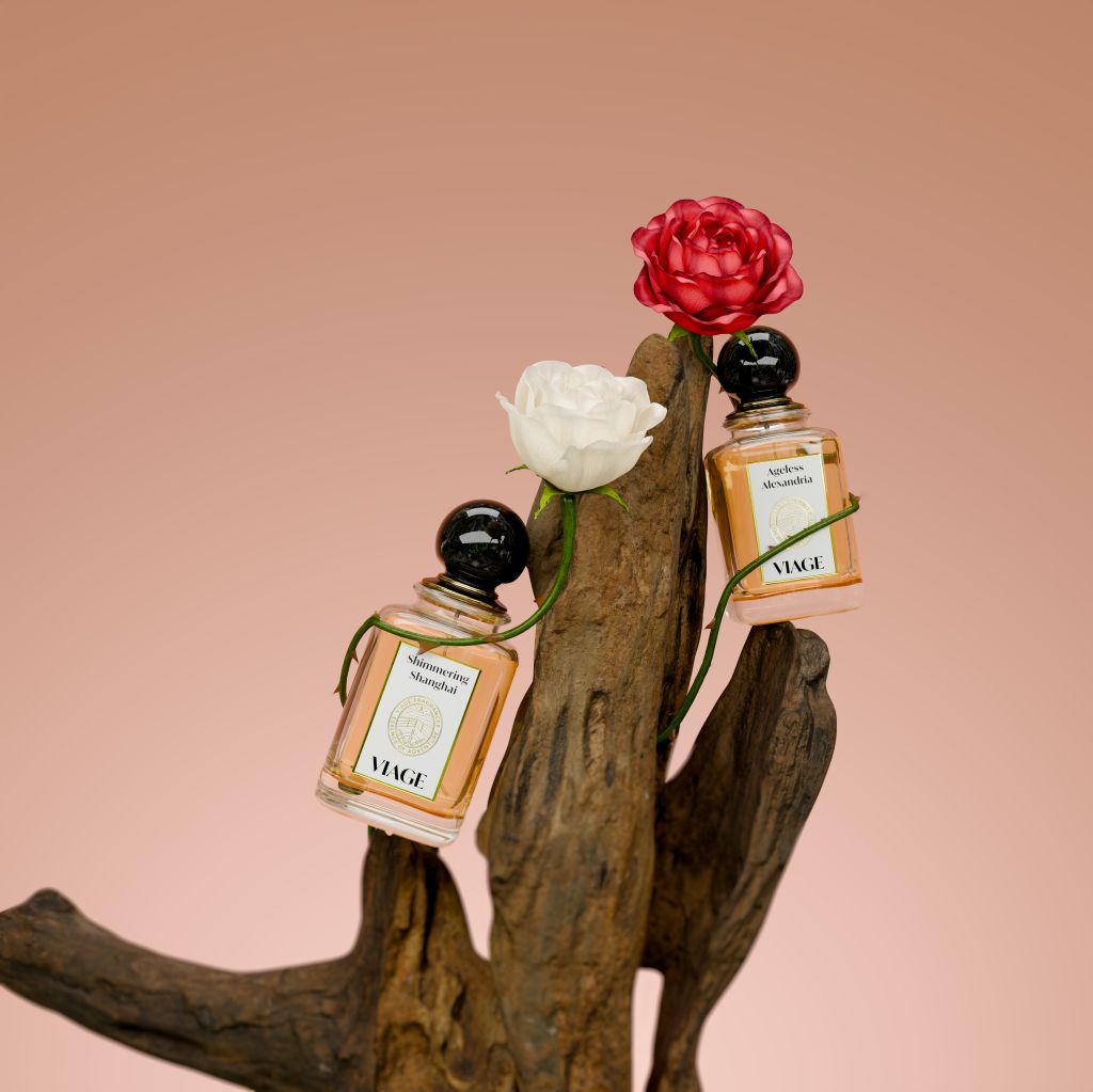 Viage Shimmering Shanghai Extrait de Parfum 100 ml – Zwei Flakons mit weisser und roter Rose an Treibholz vor rosé Hintergrund