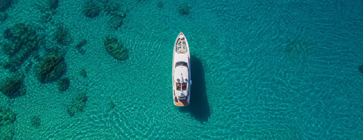 Weisse Yacht von oben auf türkisfarbenem Meer mit Felsen